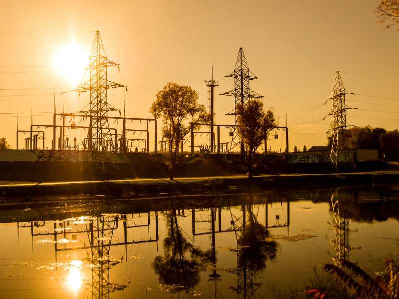 High voltage power lines and pylons on the river at sunset